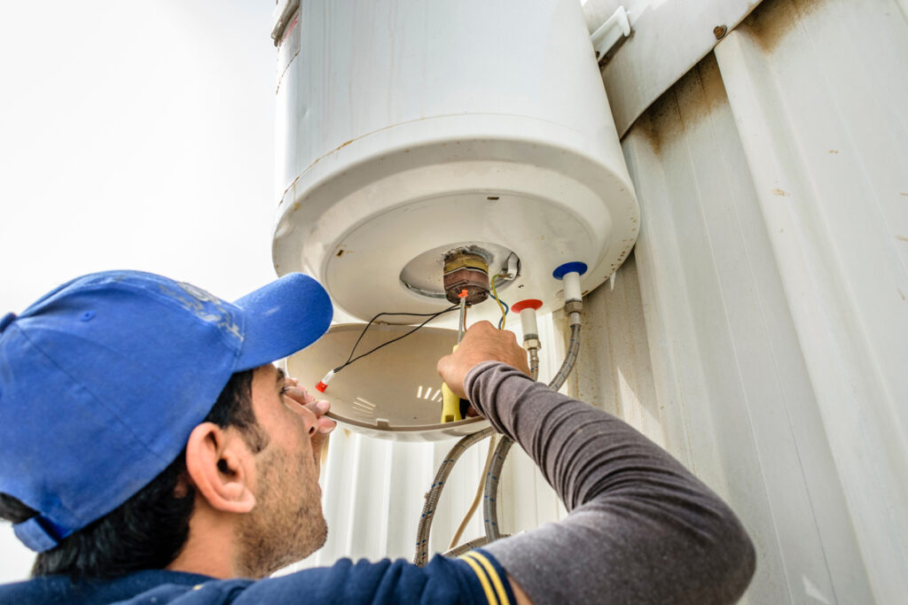 A man fixing a water heater on a wall.